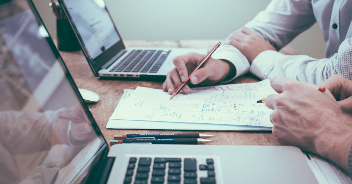 Two people collaborating over documents related to Subscription Box Marketing and laptops on a desk in an office setting.