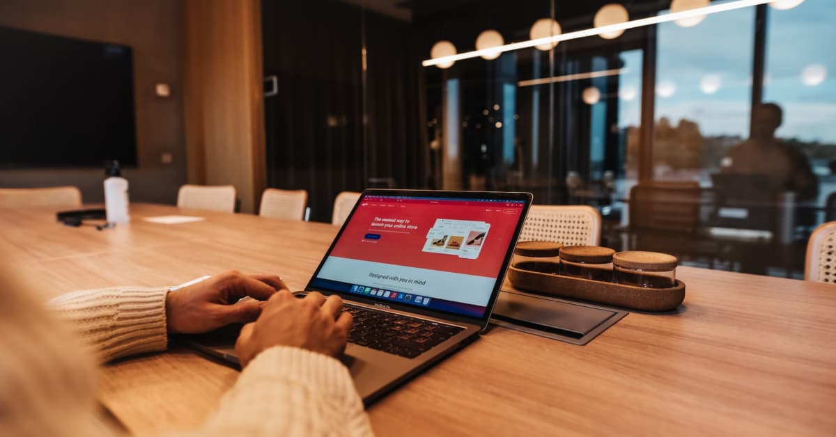 Person working on a laptop with an Ecommerce Success presentation on the screen in a modern office conference room at night.