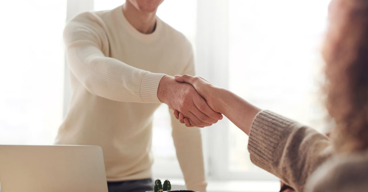 Two individuals shaking hands across a desk in a bright office setting, emphasizing the start of a subscription-based loyalty program.