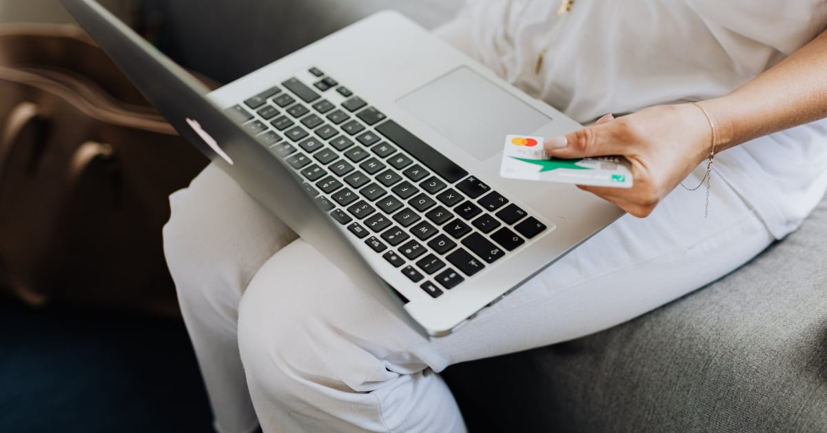 Person shopping online on an ecommerce platform using a laptop and holding a credit card.