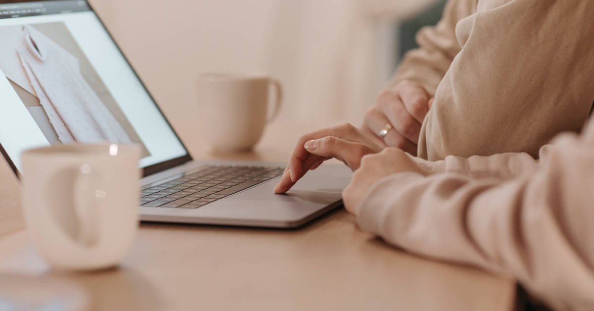 Two people in casual attire working on affiliate marketing strategies on a laptop together at a wooden table with coffee cups nearby.