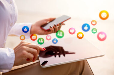 A person engages with social media, using a tablet surrounded by floating icons like likes and messages, while holding a smartphone in the other hand. This illustrates modern content marketing strategies and examples of how technology is shaping communication.
