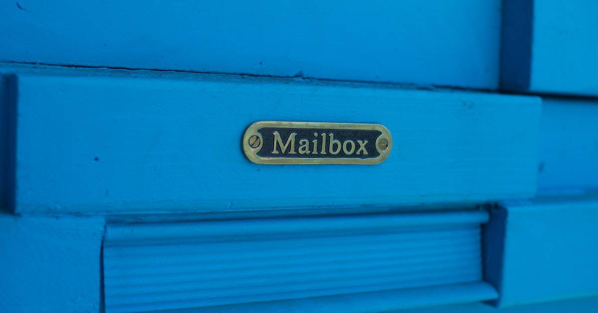 Close-up of a blue mailbox with a brass label that reads "Mailbox," showcasing the potential of direct mail marketing and its business benefits.