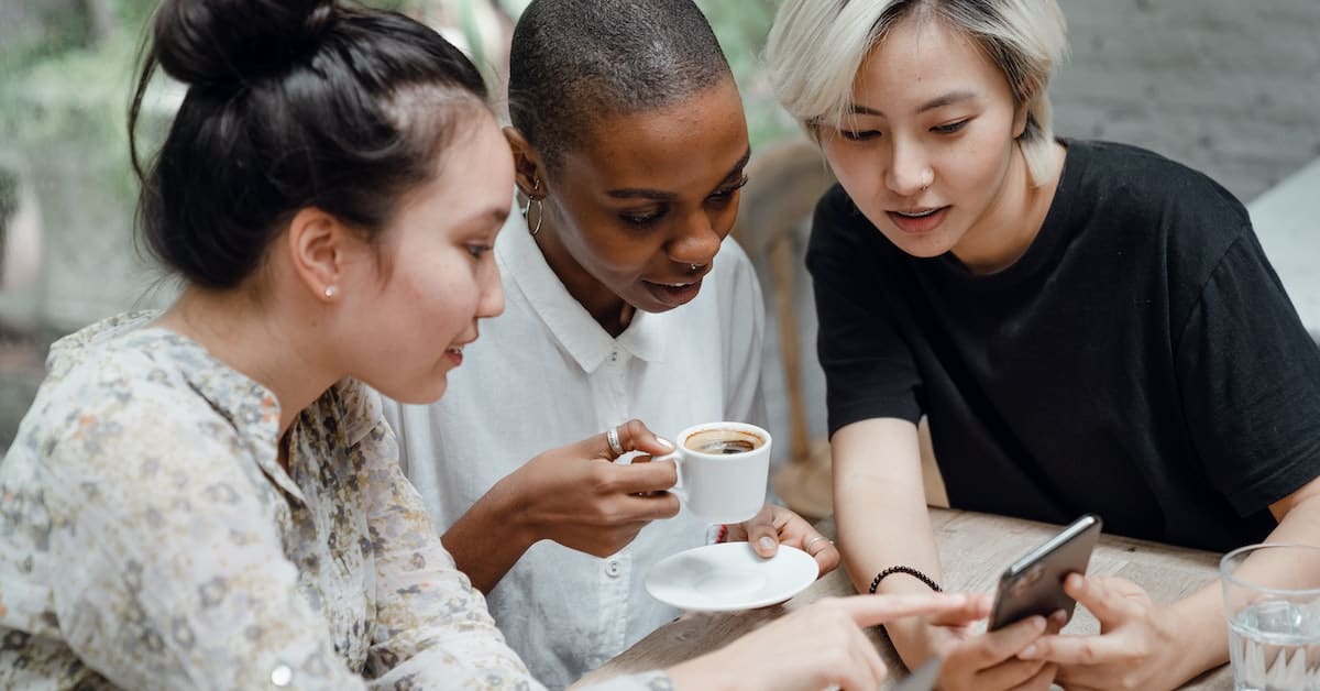 Three people are sitting at a table. One person holds a cup of coffee, while another shows something on a phone. They are in conversation and appear to be engaged with the phone screen, likely discussing key insights into ecommerce brands and strategies for building brand loyalty.