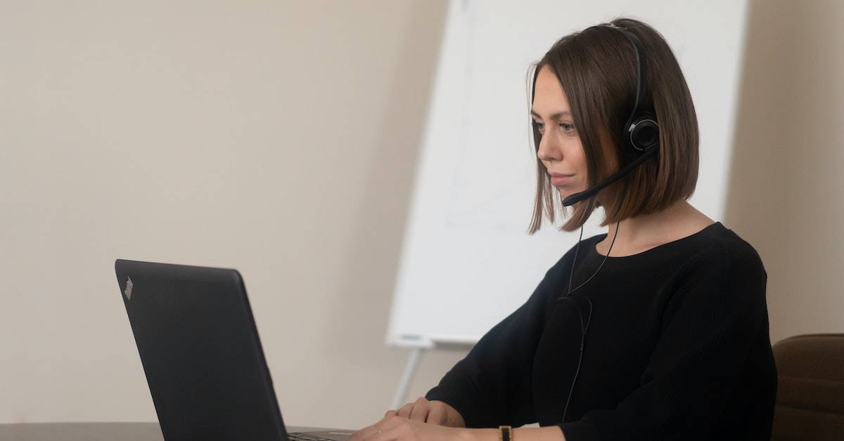 A woman wearing a headset focuses on her laptop, reviewing a Bank of America chargebacks guide in a lightly colored office.