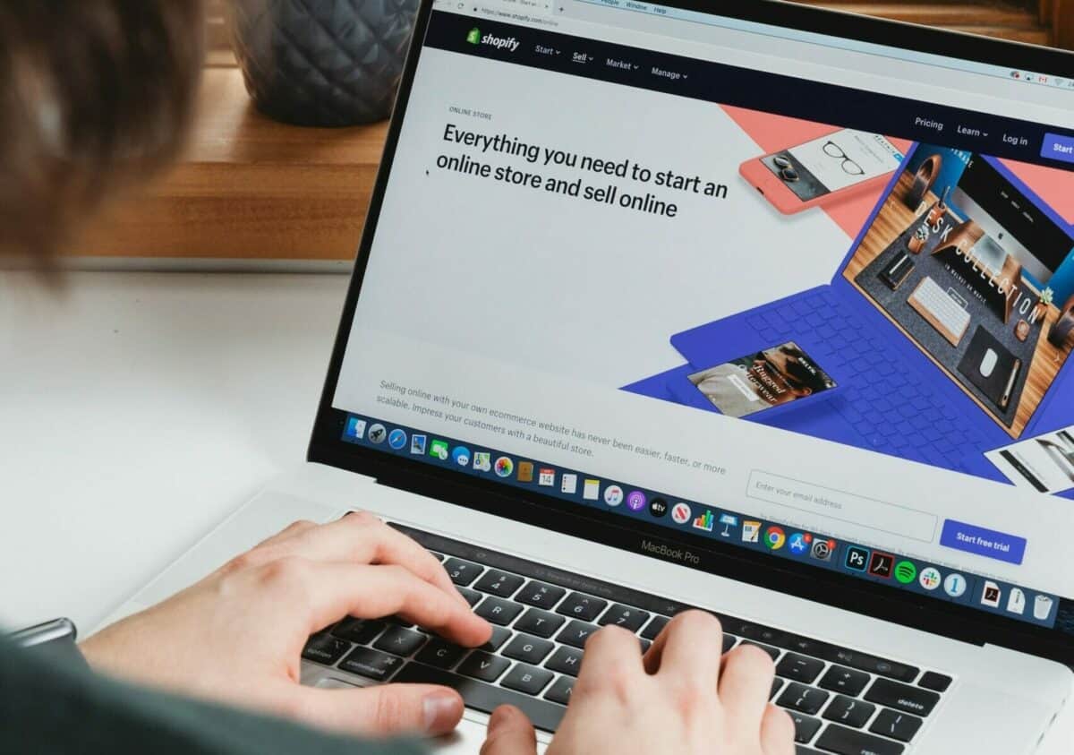 A person types on a laptop displaying the Shopify website homepage, which promotes starting an ecommerce business and selling products online.