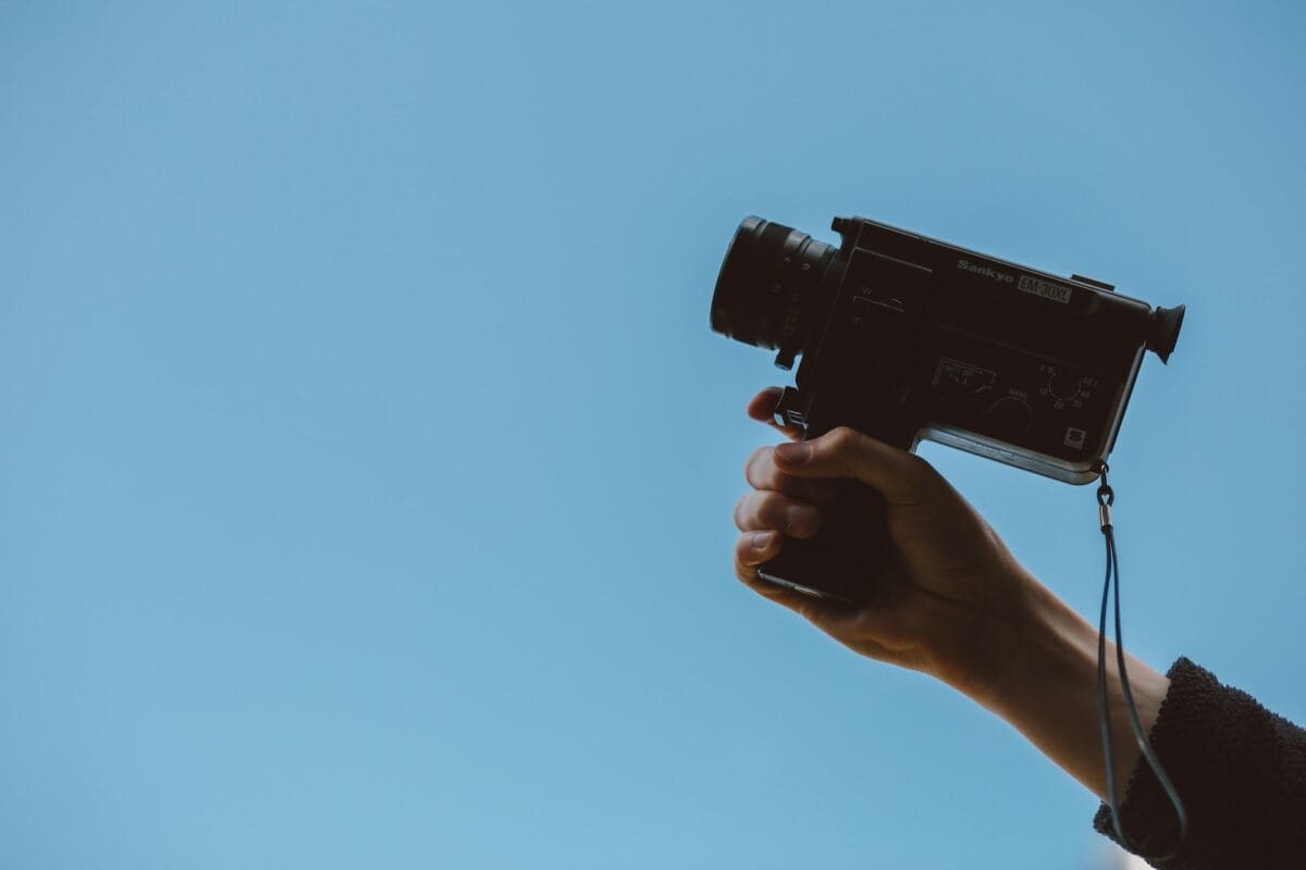 A hand holding a vintage camera against a clear blue sky, demonstrating effective video translation techniques.