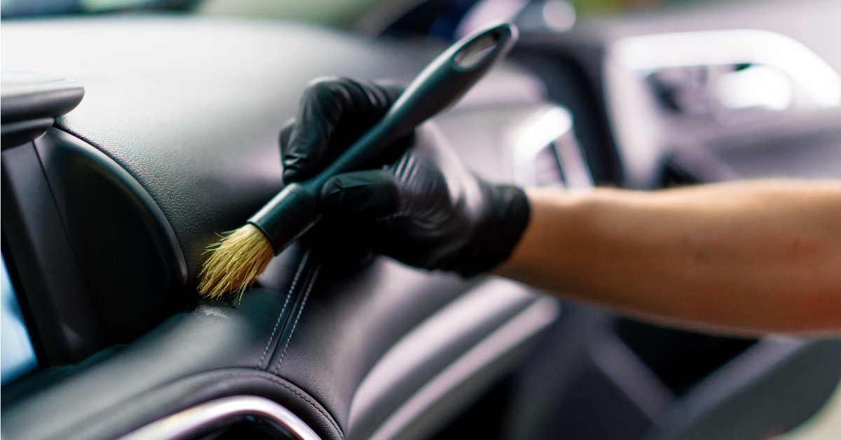 A person in black gloves uses a brush for interior maintenance to clean the inside of a car.
