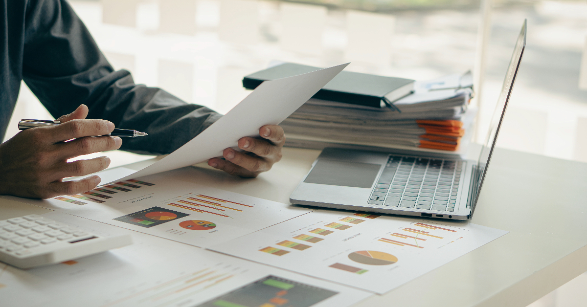 A person reviews documents and charts at a desk with a laptop, calculator, and stacked folders, analyzing the psychology of consumer behavior to better understand user intent in online marketing.