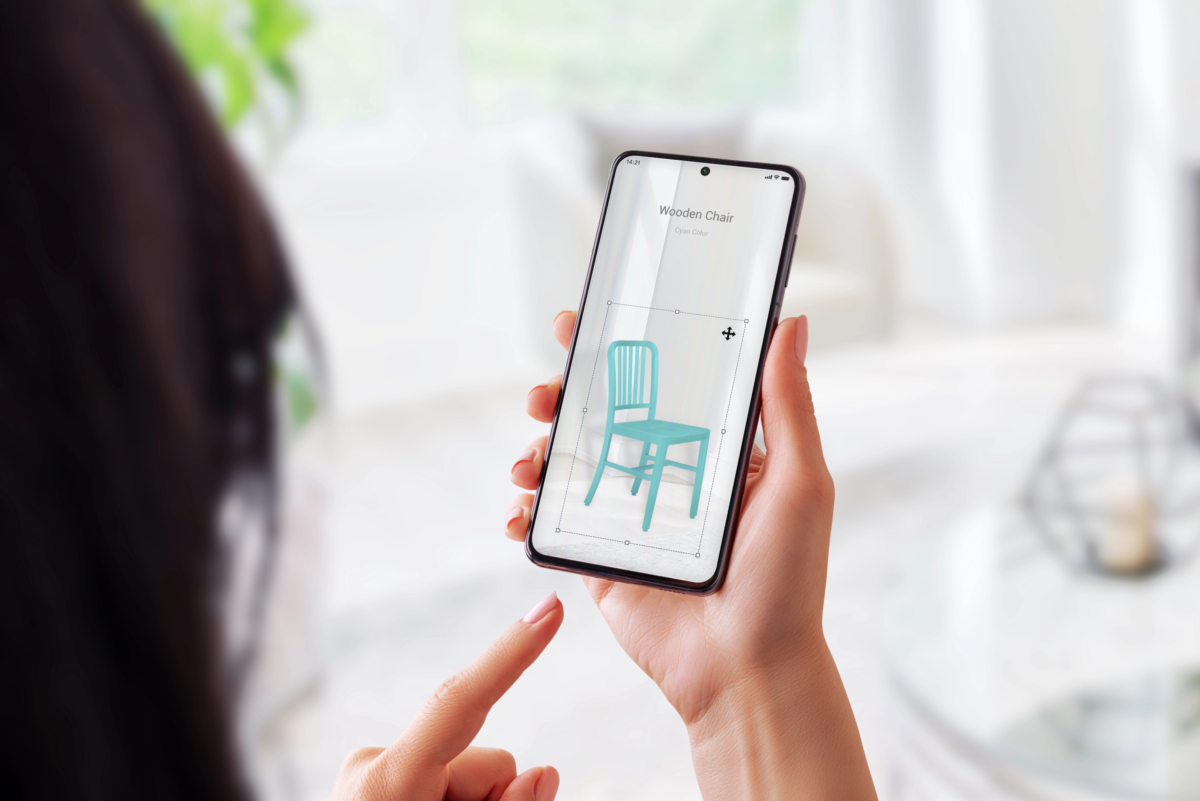 Person holding a smartphone displaying a teal wooden chair on the screen in an augmented reality app, with their index finger pointing towards it, showcasing how Shopify Furniture Store offers an innovative shopping experience with essential tips for 2023.
