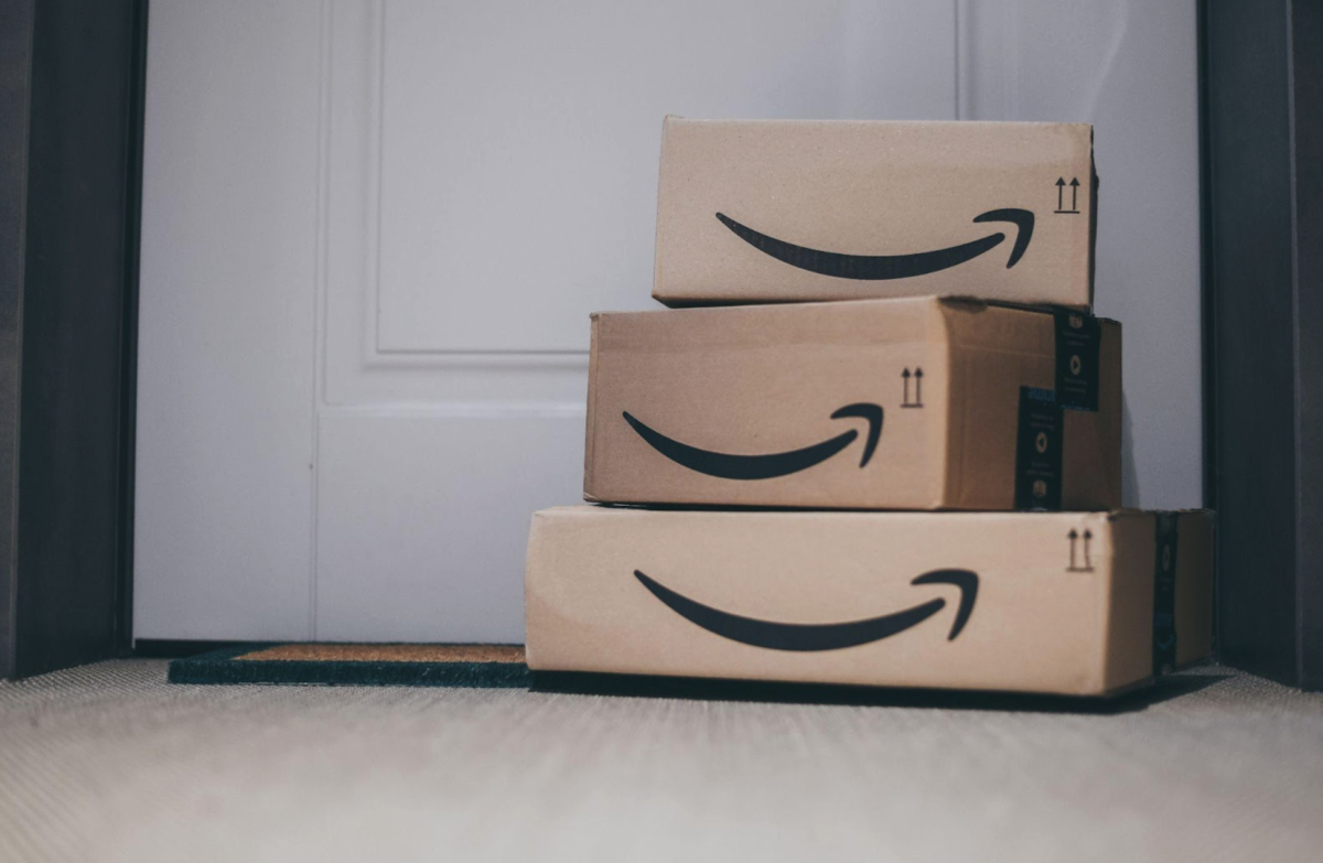 Three Amazon packages are stacked in front of a closed door, placed on a doormat, perfectly aligned with your Amazon account address.