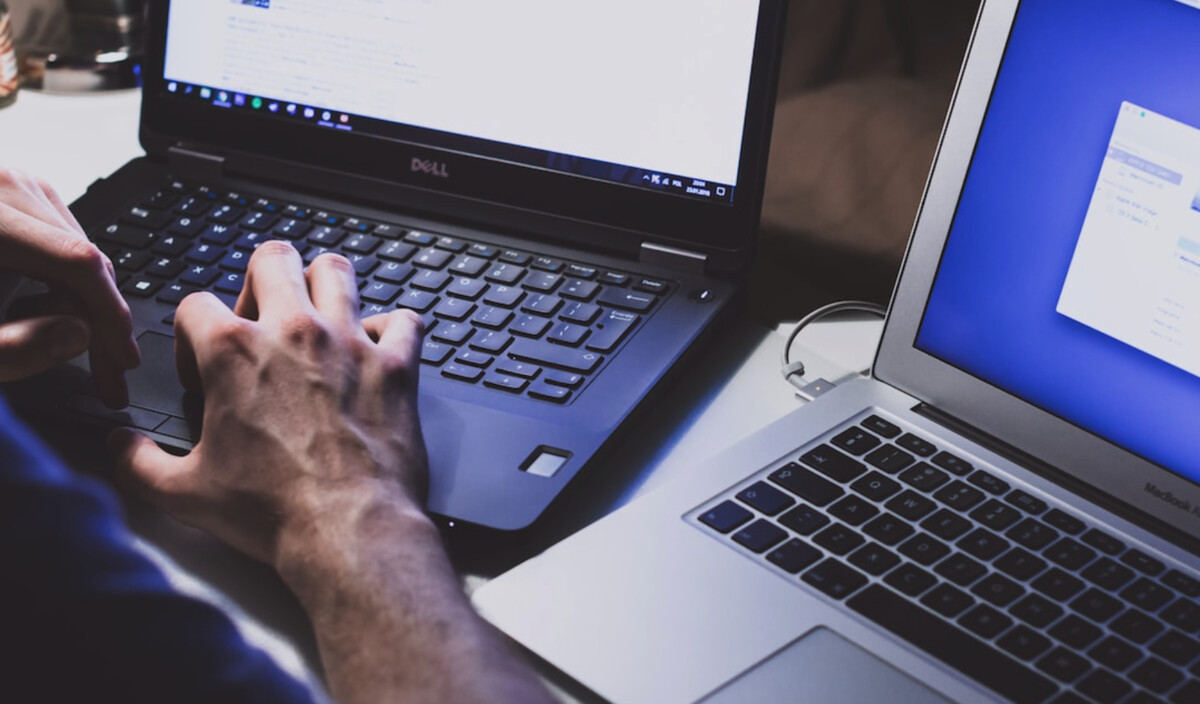 A person typing on a Dell laptop next to another open laptop with a blue screen, utilizing guide tools for Professional Services Automation.