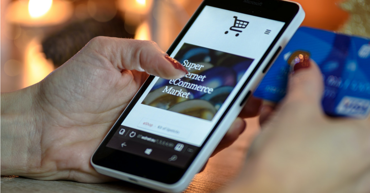 A person uses a smartphone to browse an online marketplace while holding a blue credit card, adapting shopping habits in the wake of COVID-19.