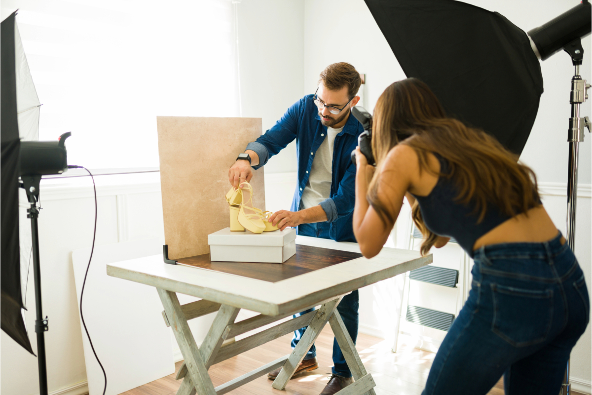 A man adjusts a high-heeled shoe on a table while a woman takes a photo of it in a studio with professional lighting, following expert product photography tips.