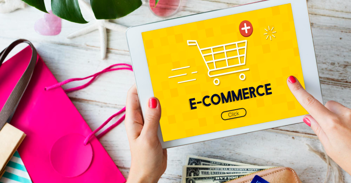 A person holds a tablet displaying an e-commerce screen and clicks a "Click" button. Nearby are a pink shopping bag, a smartphone with cards, and some dollar bills on a wooden surface—everything you need for the ultimate guide to the best ecommerce platforms of 2023.