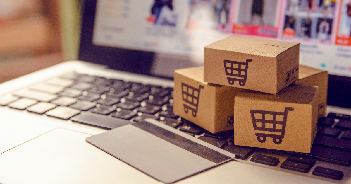 Three small cardboard boxes with shopping cart icons sit on a laptop keyboard next to a credit card, perfectly illustrating e-commerce conversion in online shopping.