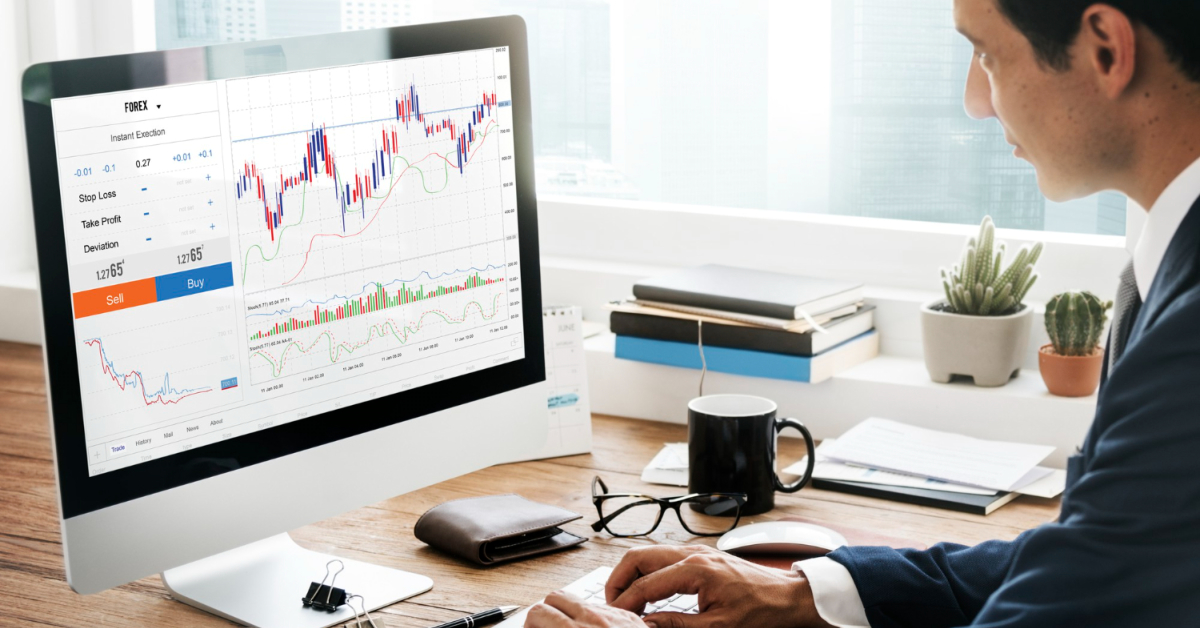 A person in formal attire analyzes stock market data on a computer screen at a desk, with graphs and trading options prominently displayed. Books, a plant, and other office items are also on the desk. They're reviewing steps for starting a Forex brokerage to better understand market trends.