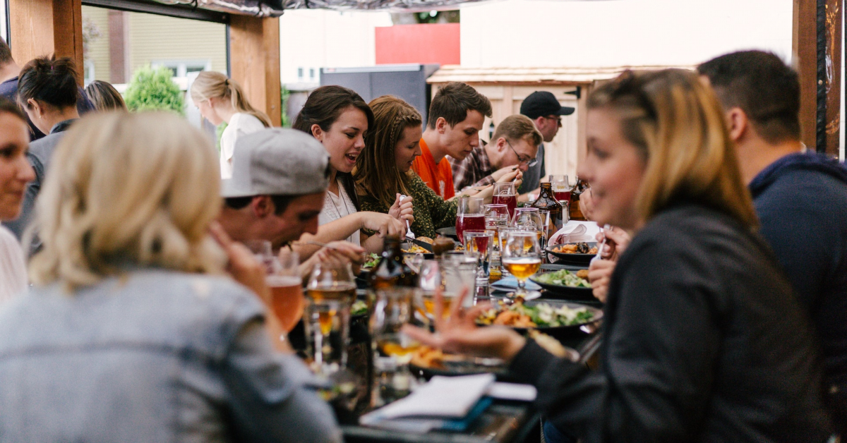 A group of people sits around a table outdoors, enjoying food and drinks while engaged in conversation about the latest restaurant loyalty programs.