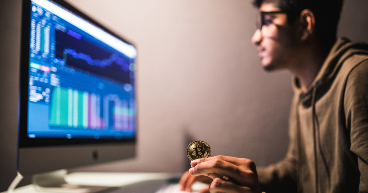 A person holding a Bitcoin in front of a computer screen displaying financial charts and graphs, perhaps uncovering the role of a liquidity provider in 2023.