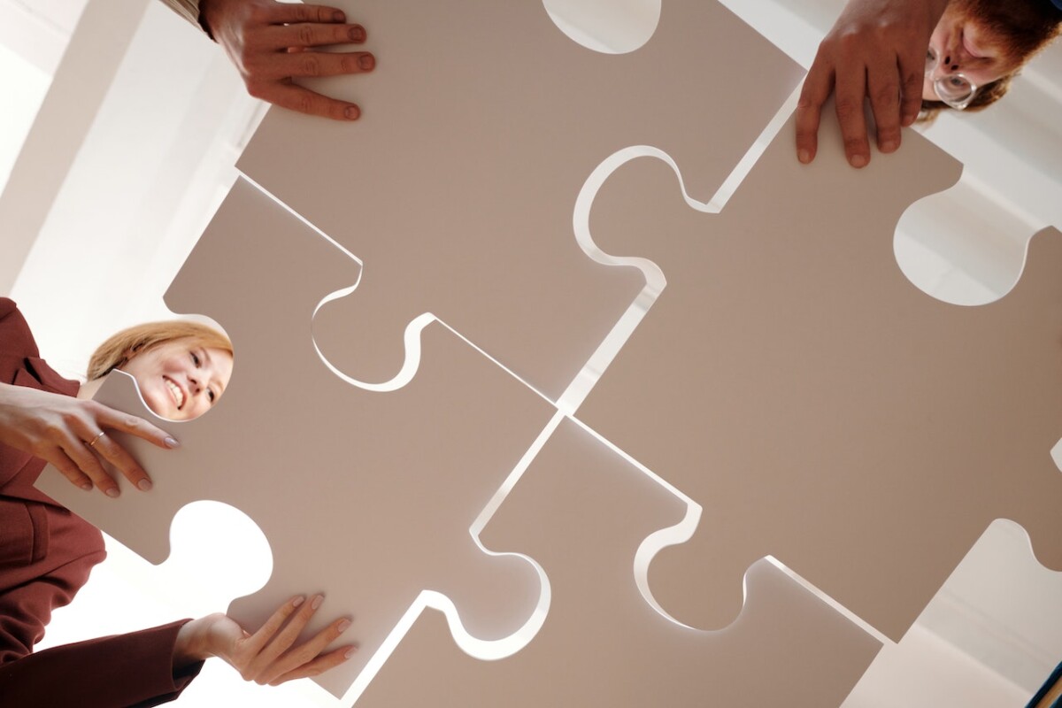 Four people are seen from below fitting large white puzzle pieces together, demonstrating effective product engagement strategies.