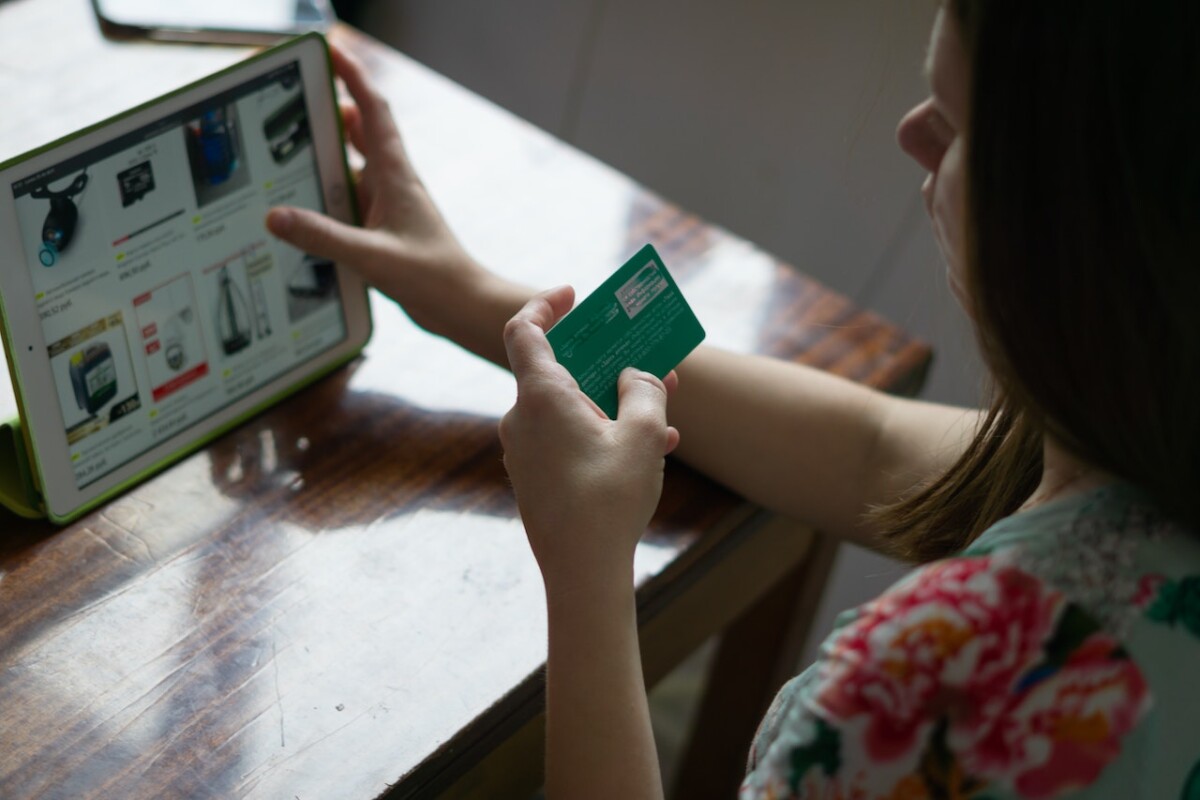 A person holding a green card is shopping online using a tablet, browsing various products on an e-commerce marketplace in 2023.