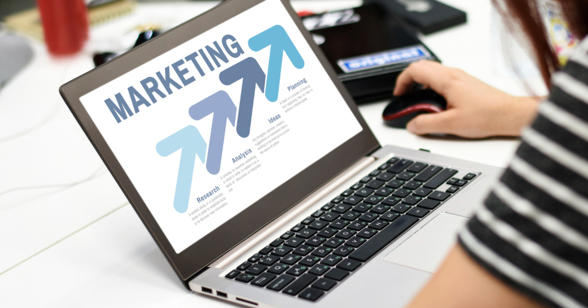 A person using a laptop with a marketing graphic displayed on the screen. The graphic contains arrows pointing upwards labeled: Research, Analysis, Ideas, Plan, and eCommerce Strategies to boost customer loyalty.