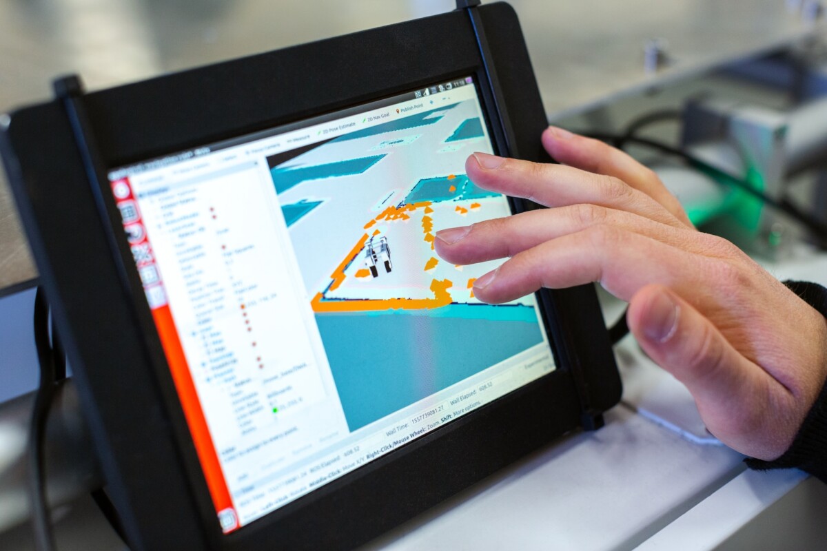 A person touches a tablet screen displaying a digital map with various colored areas and interface elements, showcasing the advanced integration of AI in software development.