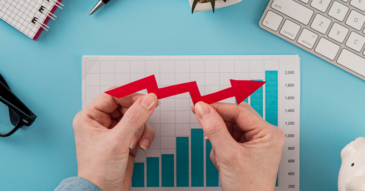 Hands holding an upward red arrow over a bar graph on a blue desk with office supplies, symbolizing how OCR software can boost efficiency in ecommerce.
