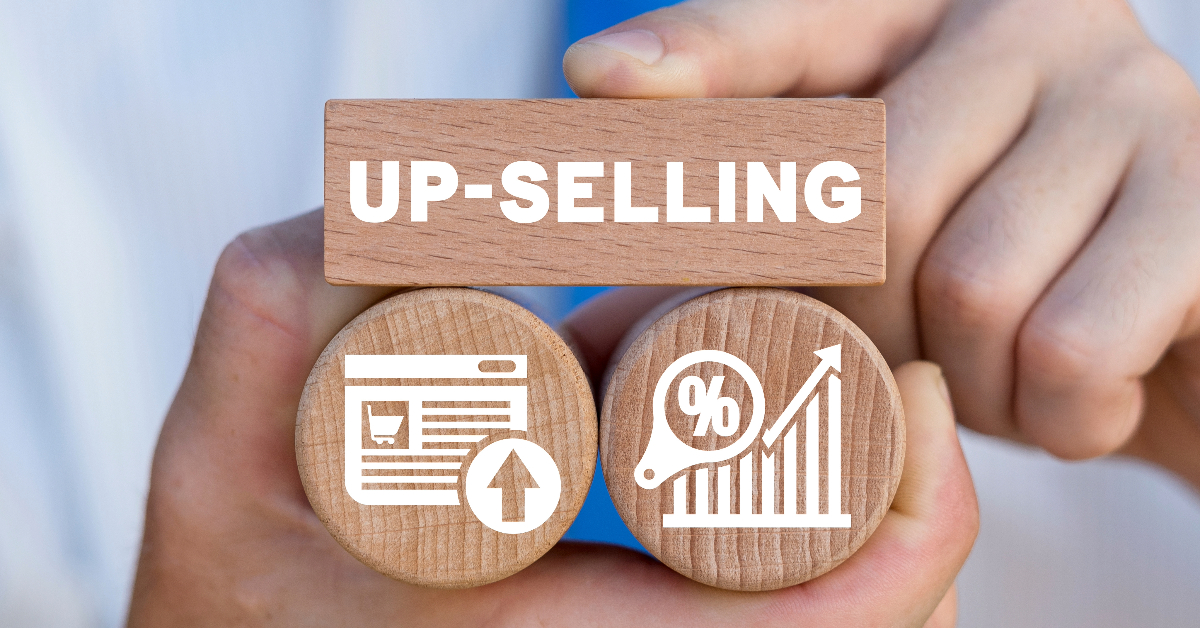 Close-up of hands holding wooden blocks with "UP-SELLING" and symbols representing online shopping and a rising percentage graph, illustrating the concept of increasing sales through upselling and effective post-purchase engagement.
