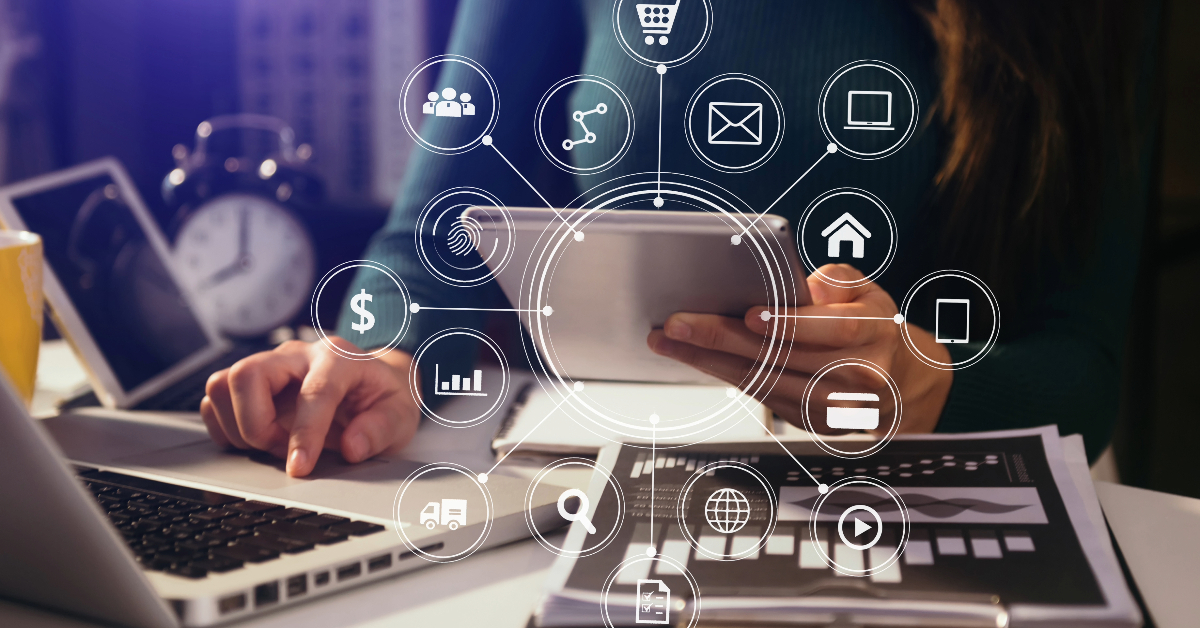 Person using a tablet and a laptop with overlay icons representing various digital functions, such as email, shopping, and analytics, suggesting a digital business environment in line with 2024 Trends.