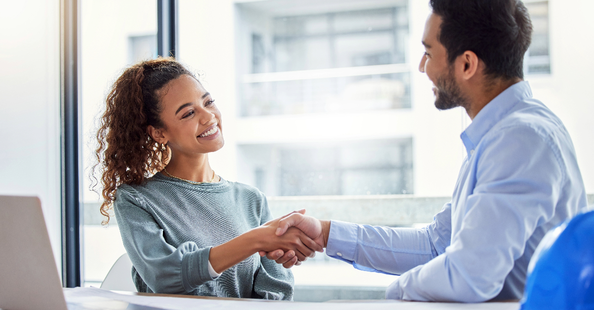 A man and woman shaking hands in an office, representing a successful B2B Commerce Cloud partnership facilitated by Salesforce.