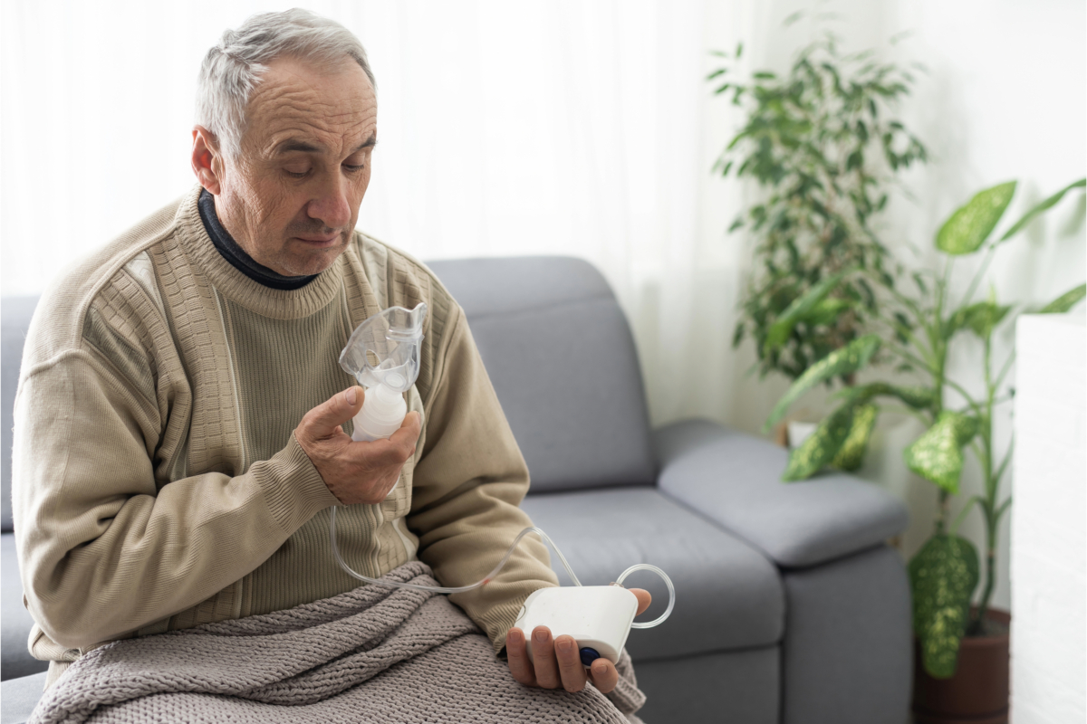 A man is sitting on a couch with the Philips SimplyGo Portable Oxygen Concentrator in his hand, maximizing its lifespan.