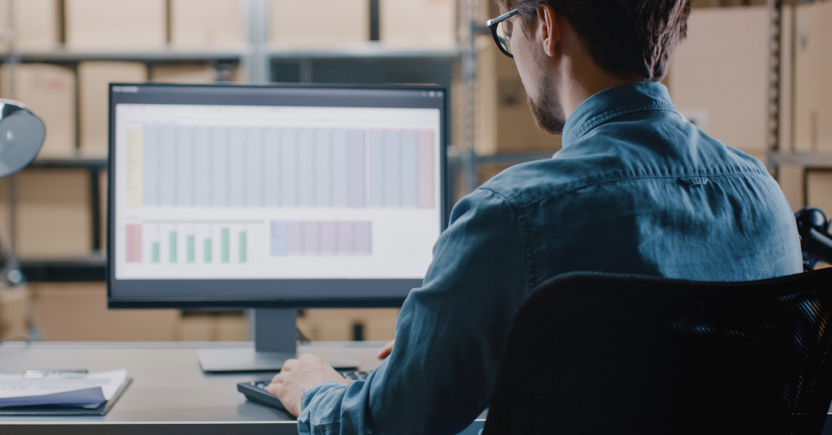 A man working on a computer in a warehouse, utilizing Amazon Price Tracking to increase e-Commerce sales.