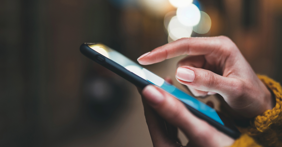A woman's hand holding a smartphone at night while using mobile app testing tools for mobile device testing.