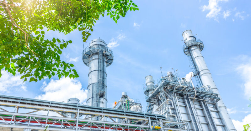 An industrial power plant contributing to a greener future with green trees and blue sky.