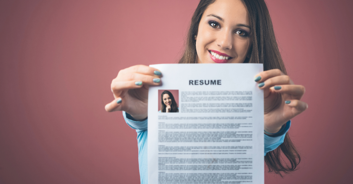 A woman is smiling and holding up a Law School resume in front of a pink background.