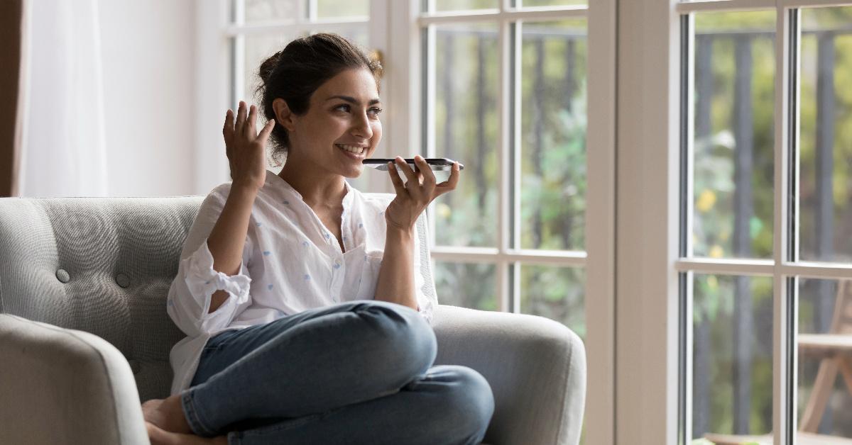 Using modern applications, a woman is sitting on a chair in front of a window, enjoying the view while her preferred choice AI voice generation system assists her.