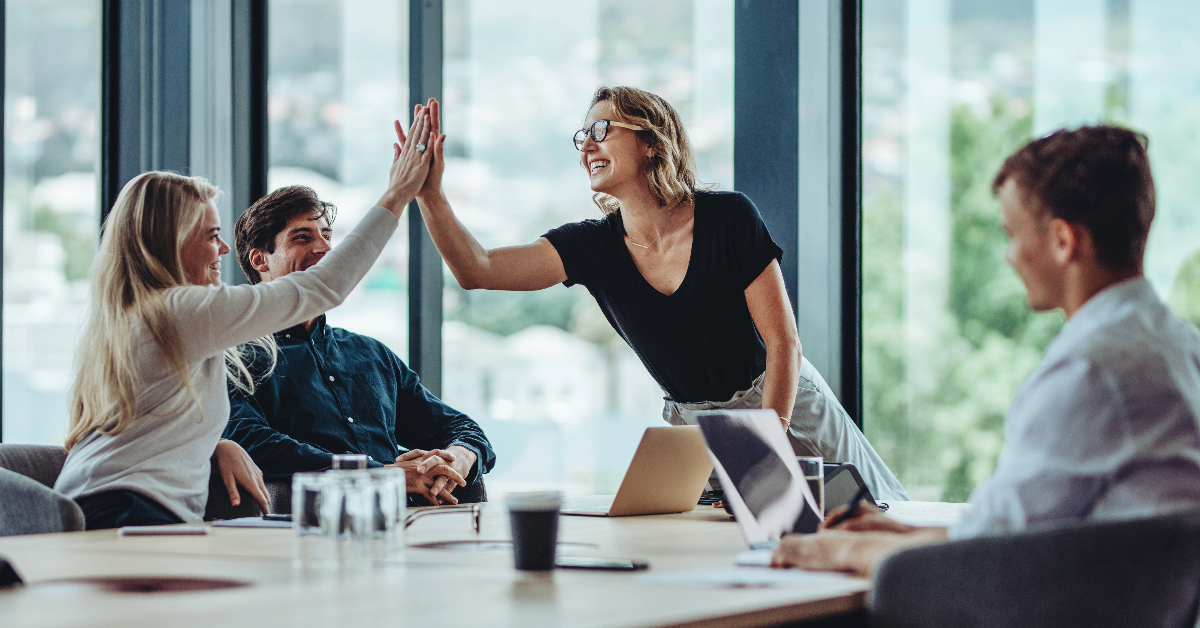 A group of business people giving each other high fives in a meeting, celebrating their sustainable success.