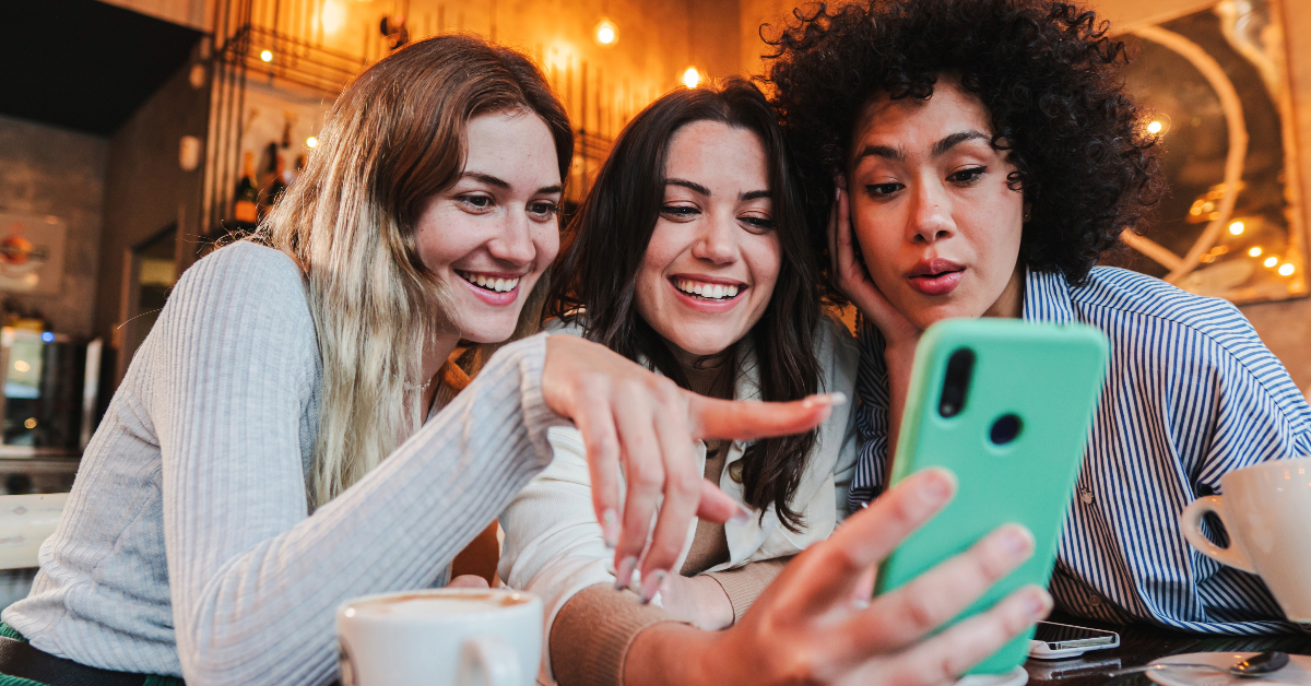 Three women are taking a selfie while sitting at a table, showcasing the latest student shopping trends in the world of e-commerce.