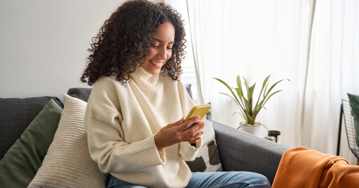 A woman is exploring rewards on mypoints.com using her cell phone while sitting on a couch.