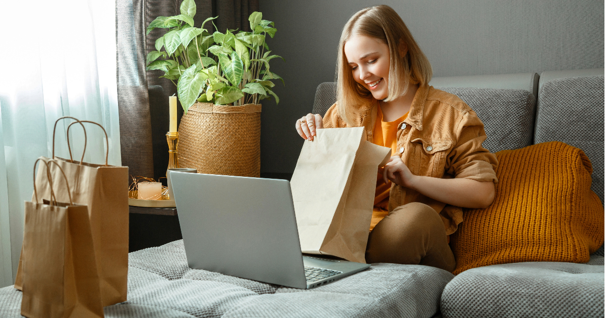 A woman engaged in online shopping, sitting on a couch with shopping bags and a laptop.