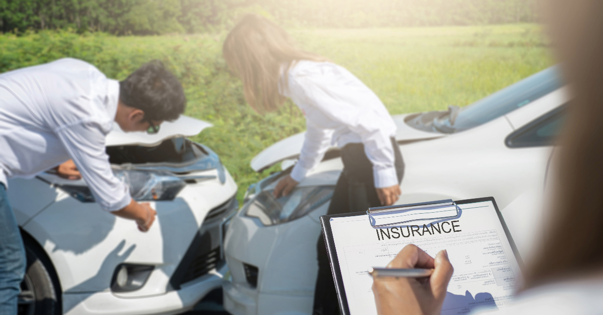 Two people inspect damage to their vehicles after a collision, with a clipboard and an insurance document prominently displayed in the foreground. This scene highlights the importance of recognizing warning signs and being prepared for any car accident, particularly when dealing with insurance companies.