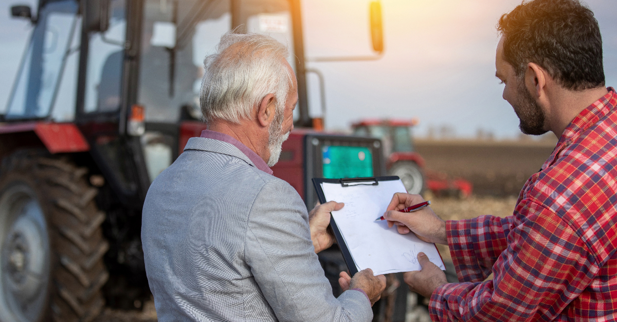 Two men standing in front of a tractor holding a clipboard discussing Farm Equipment Insurance.