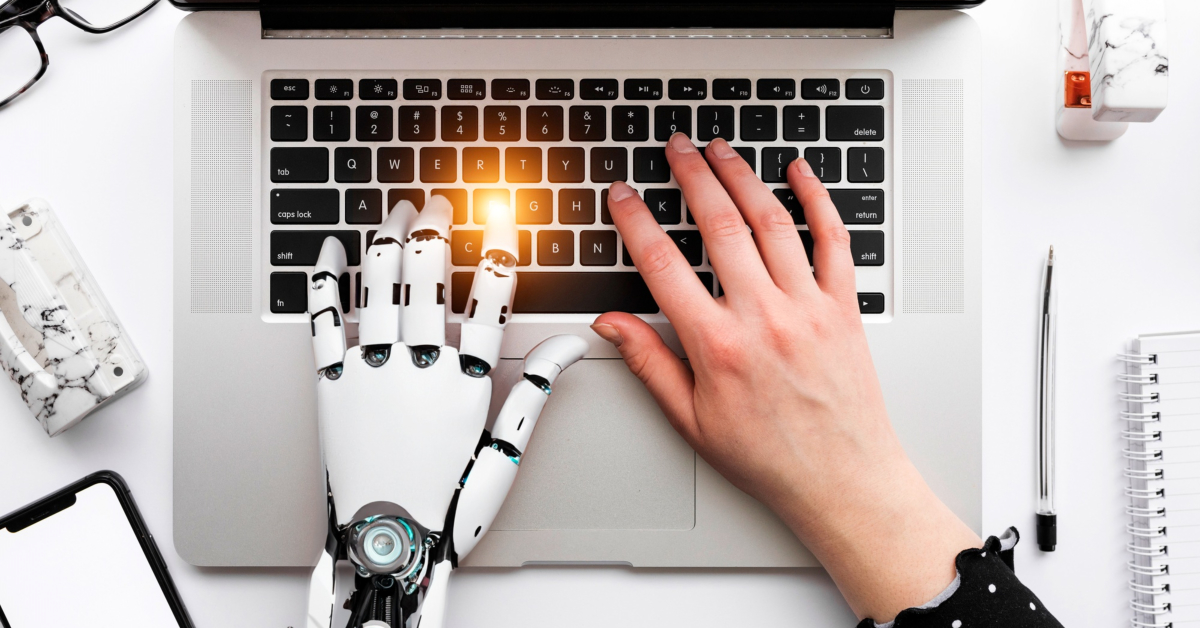 A woman using a robotic hand for automation while typing on a laptop at her company.