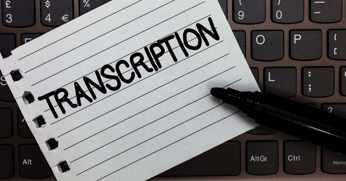 A lined notepad with the word "TRANSCRIPTION" written in bold letters is placed on a laptop keyboard, highlighting the importance of transcription services in the digital age. A black marker lies beside the notepad.
