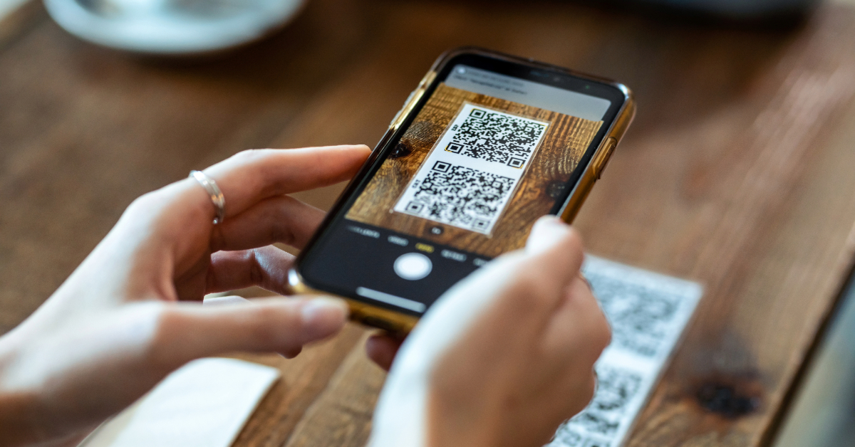 A woman is using QR Code Mastery to effectively implement asset tracking by capturing a photo of a QR code on her phone.