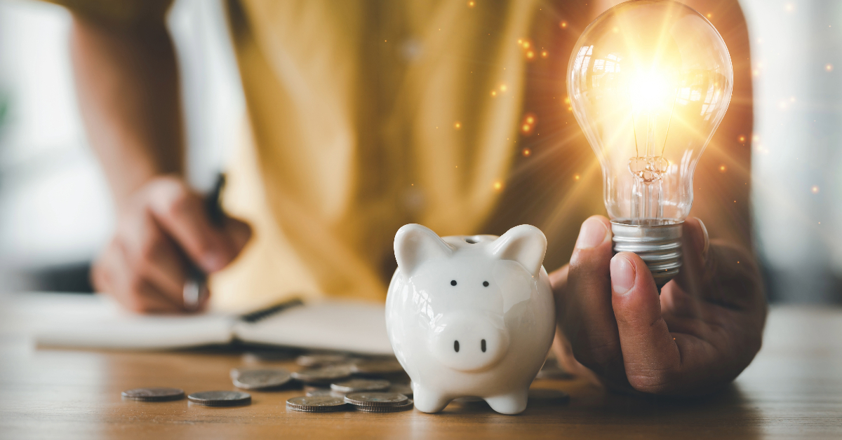 A person holding a piggy bank and an energy-saving light bulb.