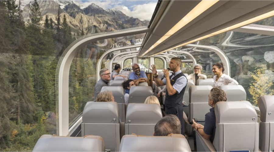 A group of people enjoying the benefits of a scenic train ride with Vancouver's stunning mountains in the background.
