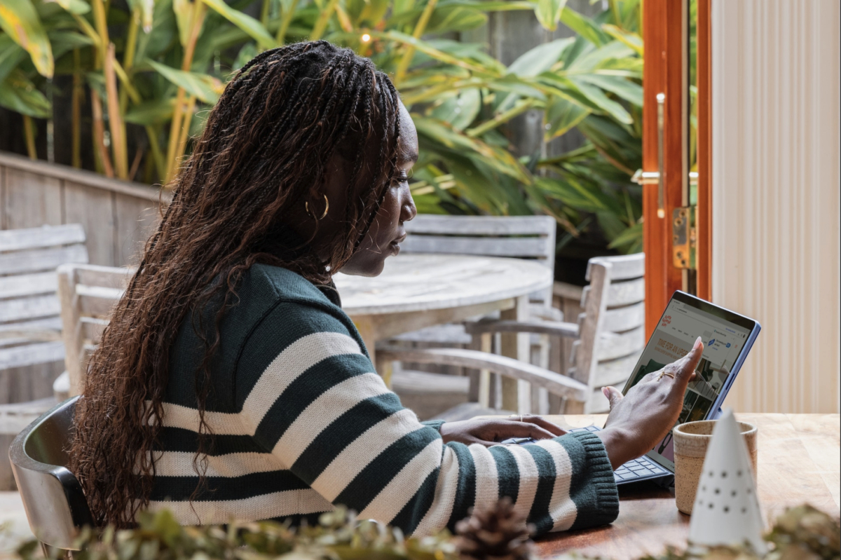 A person employs essential strategies on a touchscreen laptop at a wooden table in a garden setting, crafting success in e-commerce SEO.