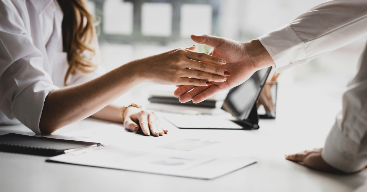 Two people from a growing company shake hands over a desk with documents and a tablet, sealing a promising deal.